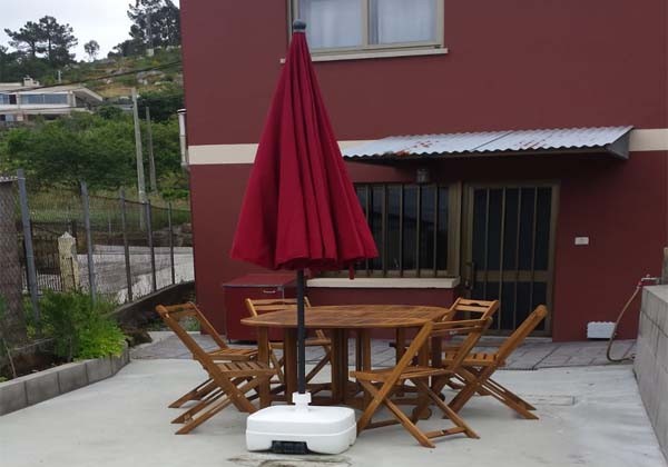 terraza con mesa y seis sillas con sombrilla, al fondo el acceso a la vivienda